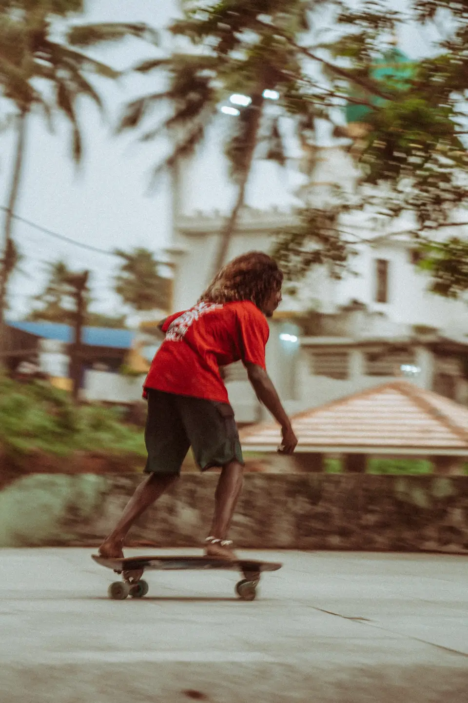A skater riding low across a concrete slope, palm trees behind